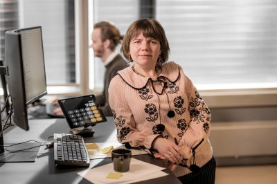 Kvinne ved arbeidspult ser inn i kamera