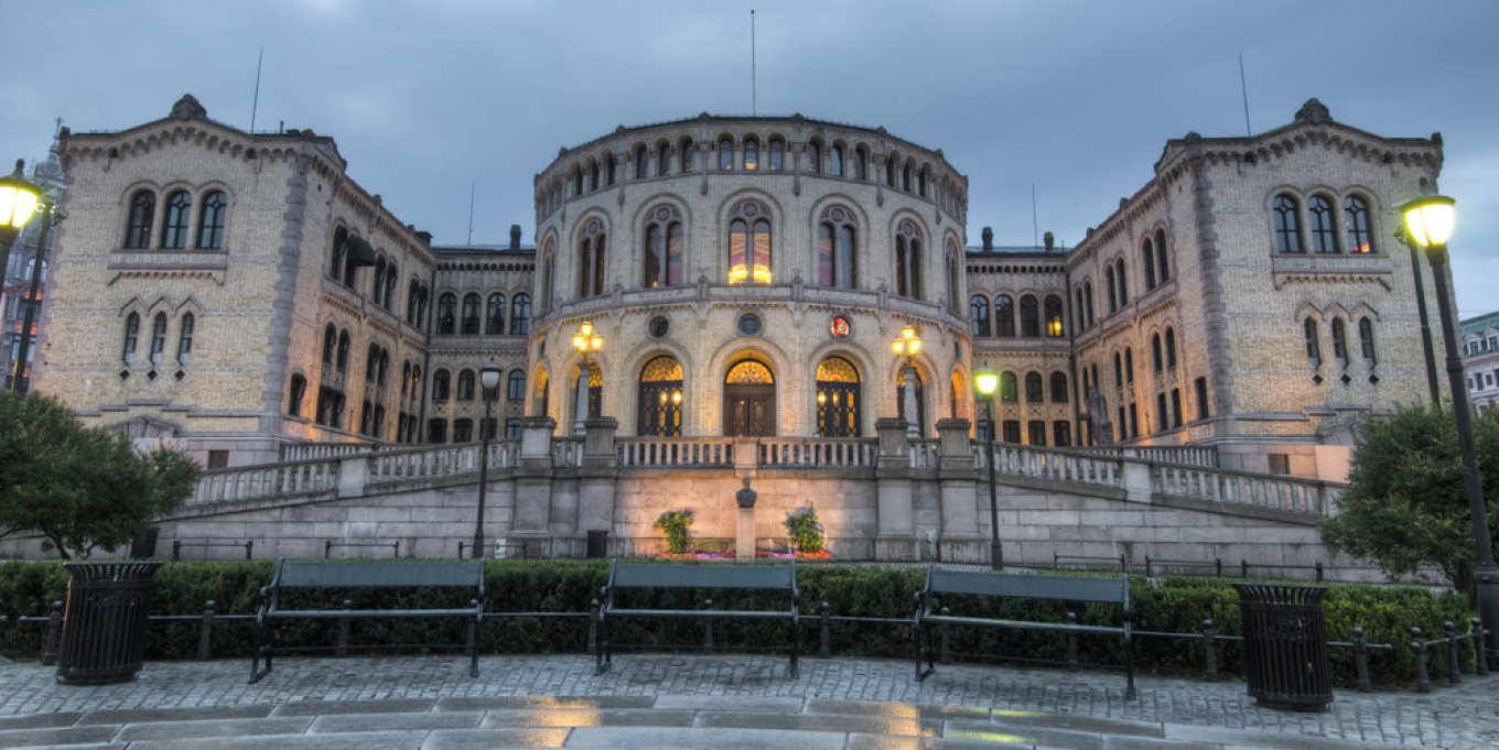 Stortingsbygningen i Oslo, opplyst om kvelden med grå himmel i bakgrunnen.