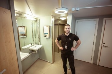 Mann i svart t-skjorte står på et moderne bad med vask og speil.