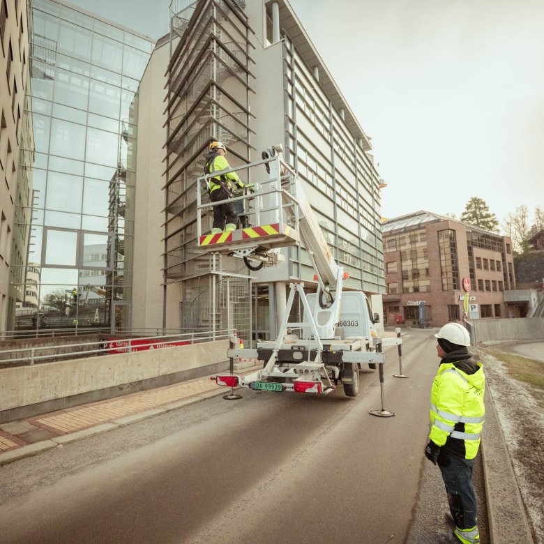 Arbeidere i lift utfører vedlikehold på en moderne bygning i et byområde.