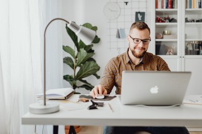 Mann jobber på laptop ved skrivebord med planter og bøker i bakgrunnen.