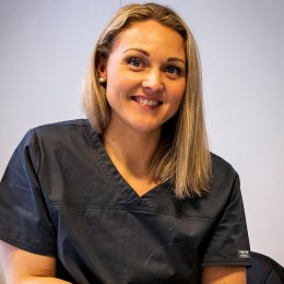 Kvinne i mørk uniform smiler mot kameraet, klar for jobb i helsevesenet.