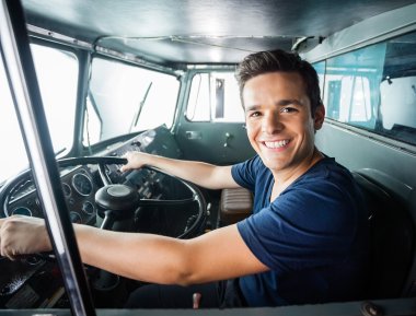 Smilende mann sitter bak rattet i en buss eller lastebil, klar til å kjøre.