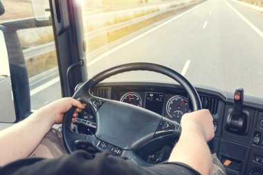Sjåfør holder rattet på en lastebil som kjører på en motorvei.