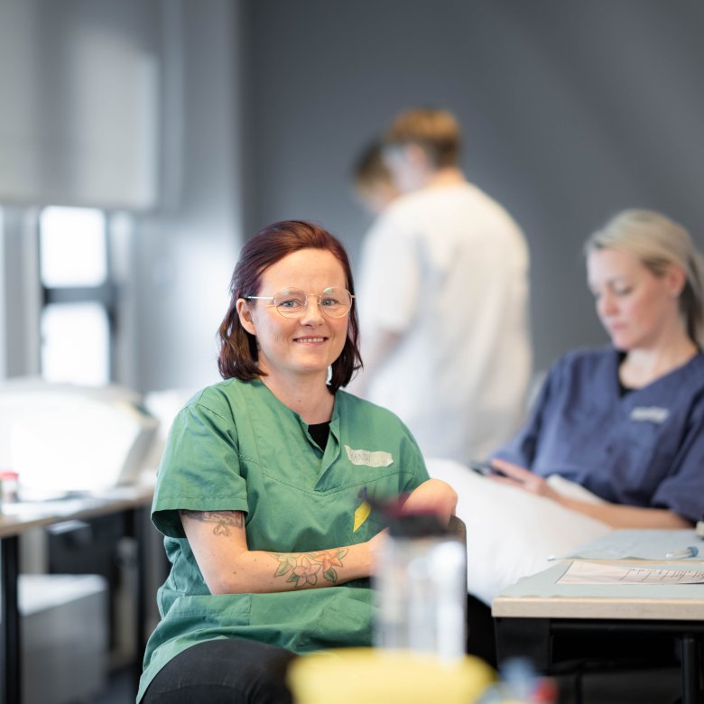 Person i grønn uniform smiler, to personer i bakgrunnen i helseuniformer.