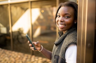 Ung kvinne smiler og holder en mobiltelefon utendørs.