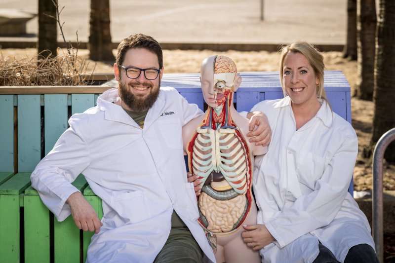 To personer i hvite frakker med anatomisk modell utendørs.